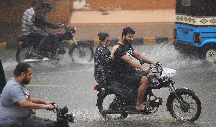 Commuters ride motorbikes along a street during a monsoon rainfall in Karachi on July 5, 2022. (AFP)