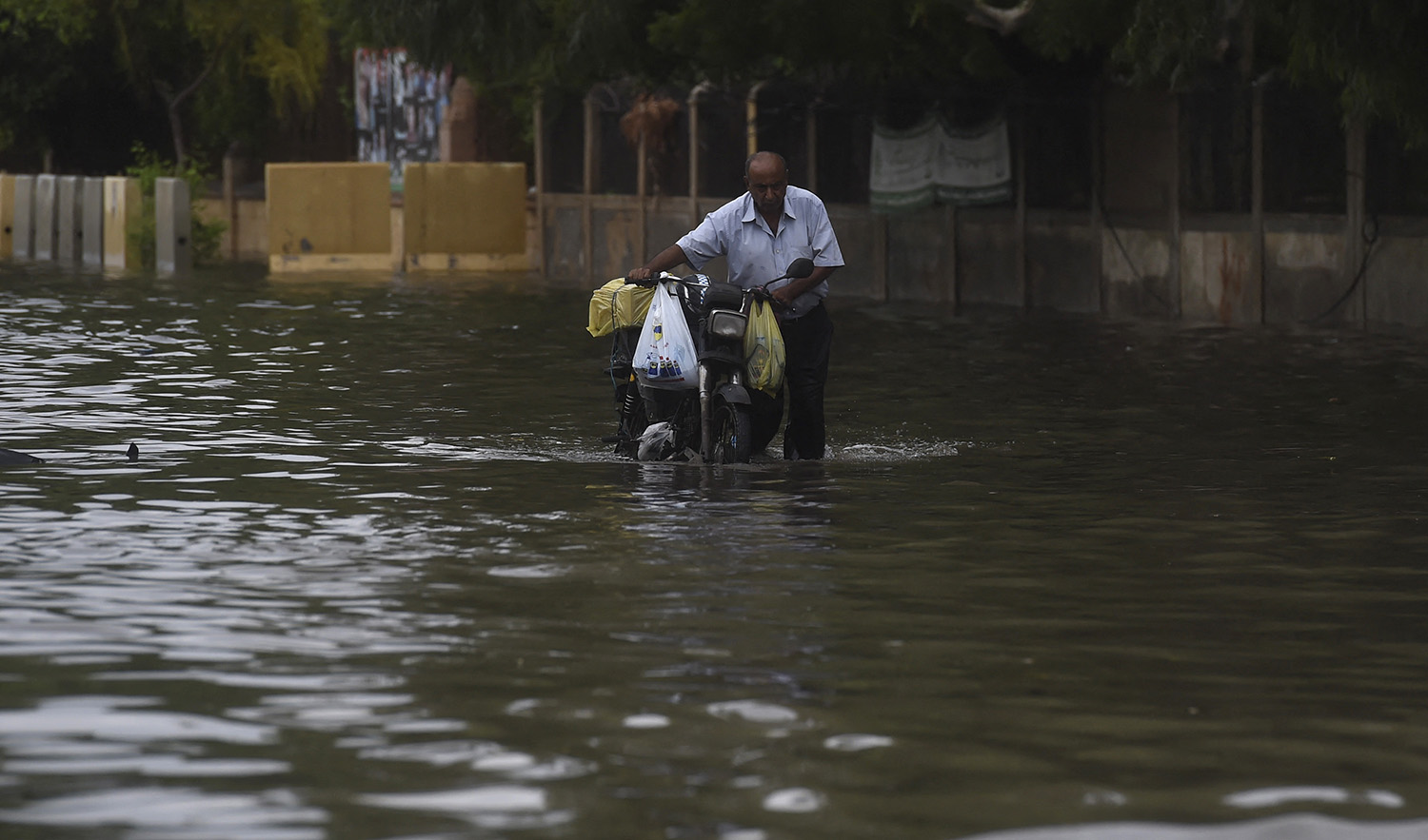 A man pushes his motorbike along a flooded street after a monsoon rainfall in Karachi, Pakistan, on July 9, 2022. (AFP)