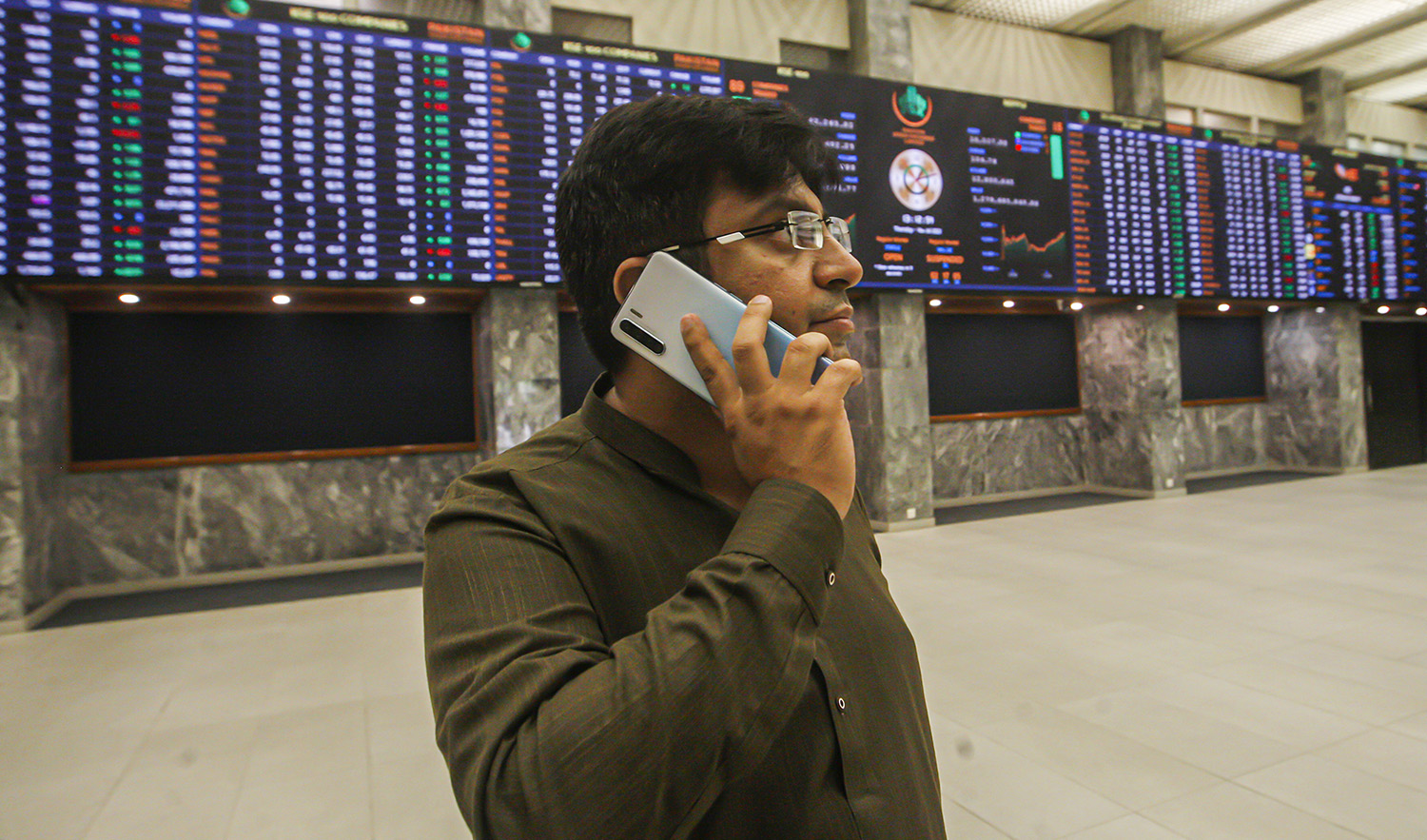 A broker talks on his cell phone while monitoring a stock index on a big screen at the Pakistan Stock Exchange, which responded positively after the news of an International Monetary Fund bailout package, in Karachi, Pakistan, on July 14, 2022. (AP)