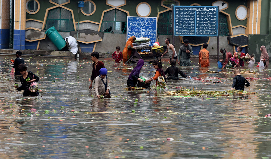 People pick vegetables from water at a flooded marketplace after heavy rainfall in Lahore on July 21, 2022. (AFP)