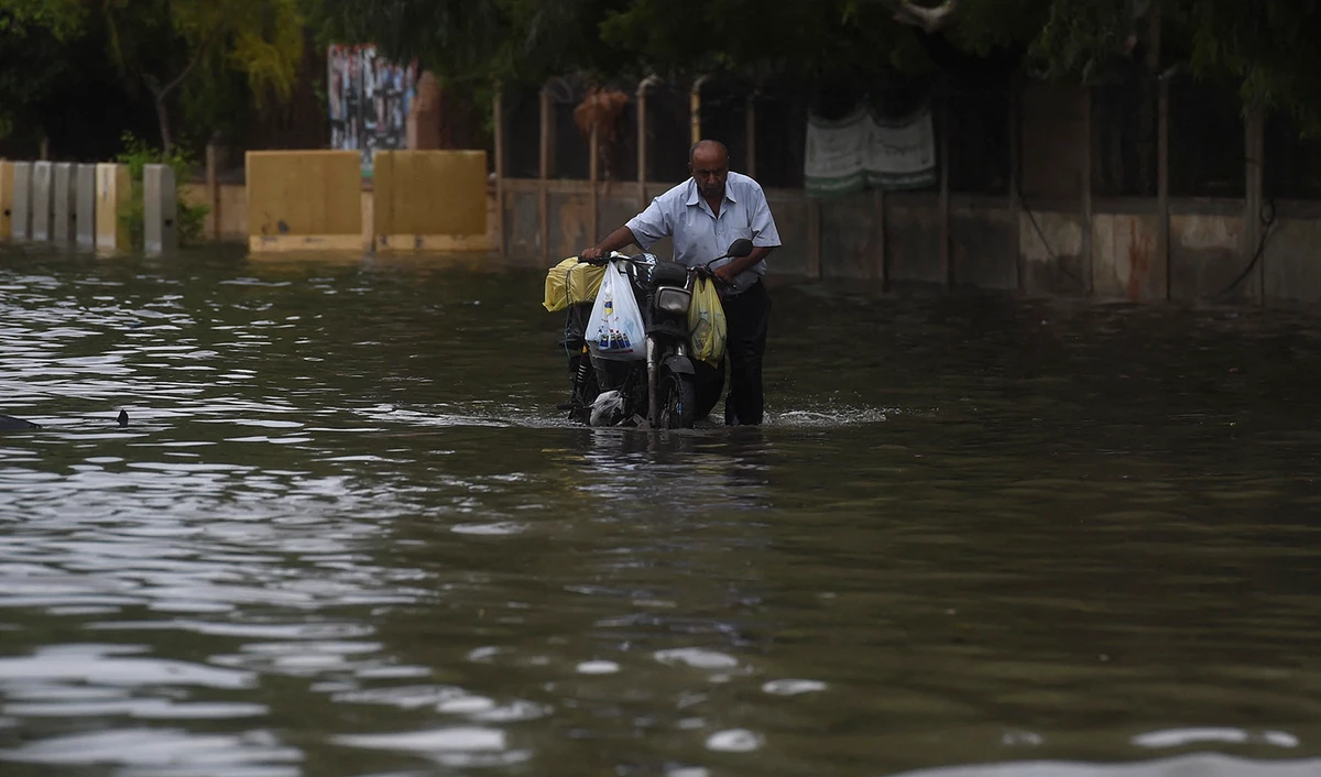 A man pushes his motorbike along a flooded street after a monsoon rainfall in Karachi, Pakistan, on July 9, 2022. (AFP)