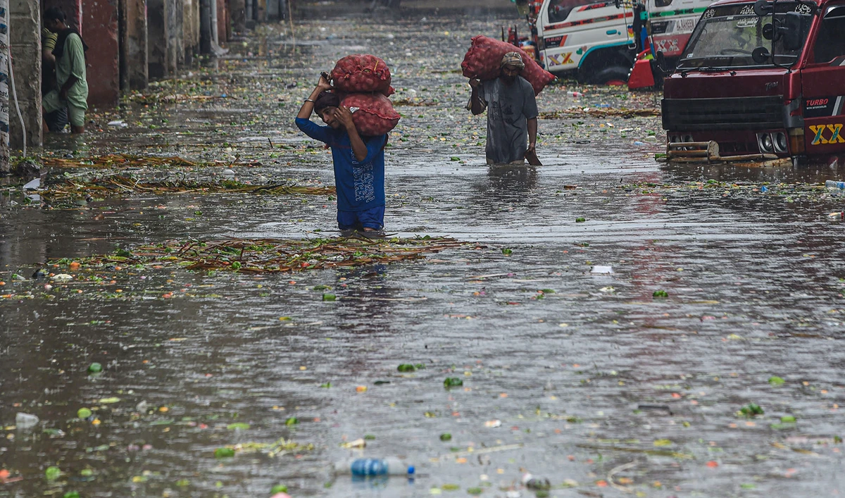 Laborers carry sacks of onions in a flooded market after a heavy rain shower in Lahore, Pakistan, on July 14, 2022. (AFP/File)