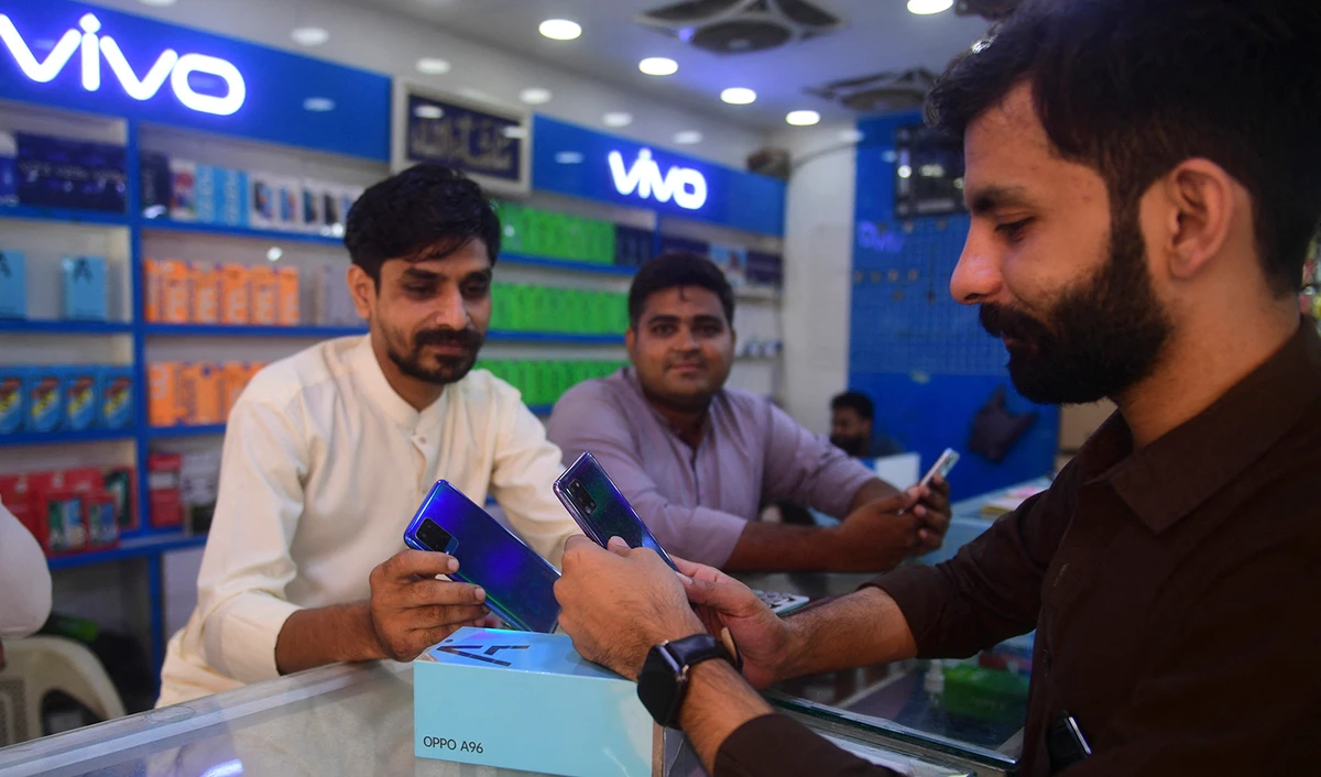 A shopkeeper shows a mobile phone to a customer at a mobile phone store in Karachi, Pakistan, on May 20, 2022. (AFP)