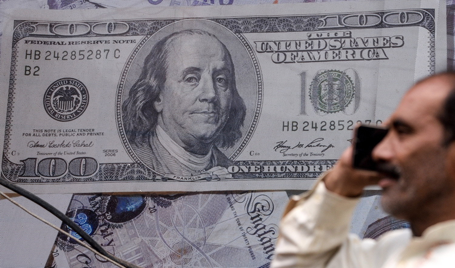 A Pakistani man talks on the phone in front of a poster displaying US dollars at the currency exchange place in Lahore on May 16, 2019. (AFP/File)