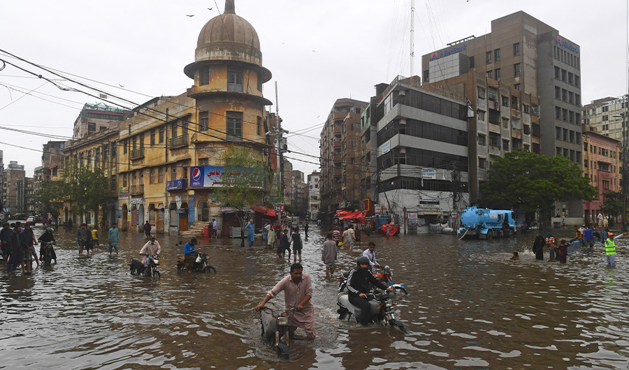 People wade across a flooded street after heavy monsoon rainfall in Karachi on July 25, 2022. (AFP)