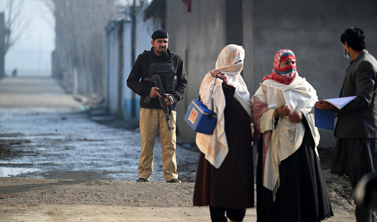 In this picture taken on January 24, 2022, a policeman (L) escorts health workers during a door-to-door polio vaccination campaign on the outskirts of Mardan, in the Pakistan's Khyber Pakhtunkhwa province. (AFP/File)