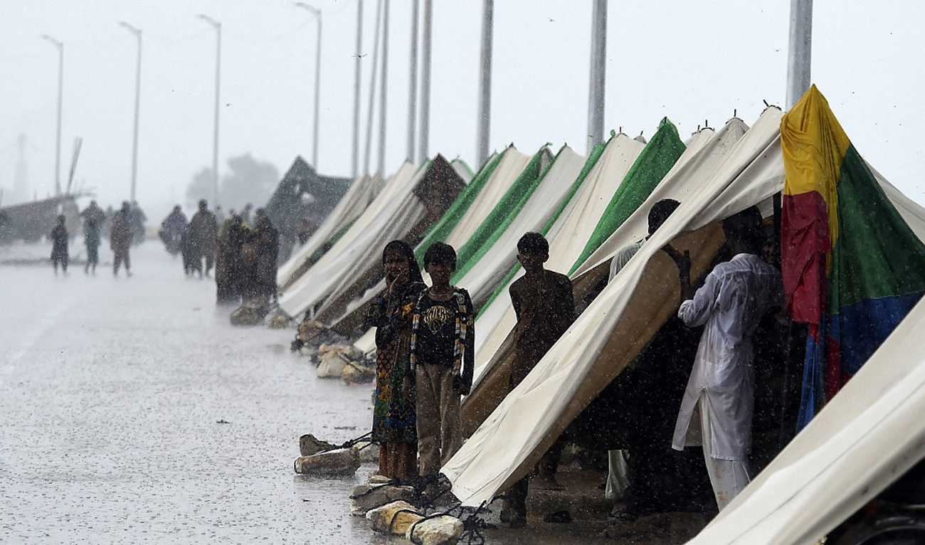 People who fled their flood hit homes stand outside temporary tents set along a road during a heavy monsoon rainfall in Sukkur of Sindh province, Pakistan on August 27, 2022. (AFP)