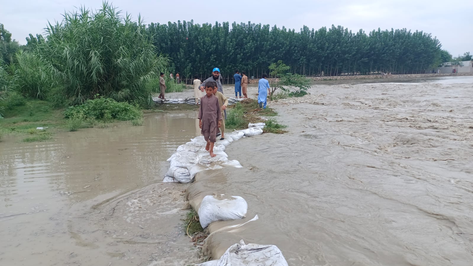 Afghan refugee children cross a flooded stream in Hajizai Refugee Camp in Charsaddah, Pakistan, on August 28, 2022. (Photo Courtesy: Ismail Khan Afghan refugee)