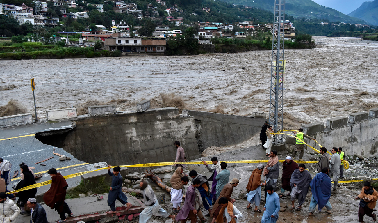 People gather in front of a road damaged by flood waters following heavy monsoon rains in Madian area in Pakistan's northern Swat Valley on August 27, 2022. (AFP)