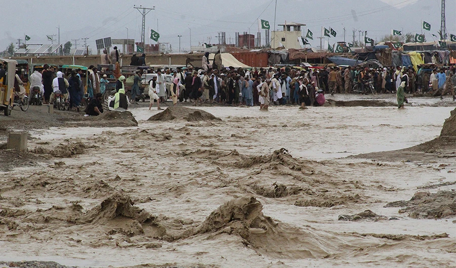 People wade through flooded mud water after heavy monsoon rainfall in the border town of Chaman in Balochistan province on August 25, 2022. (AFP)