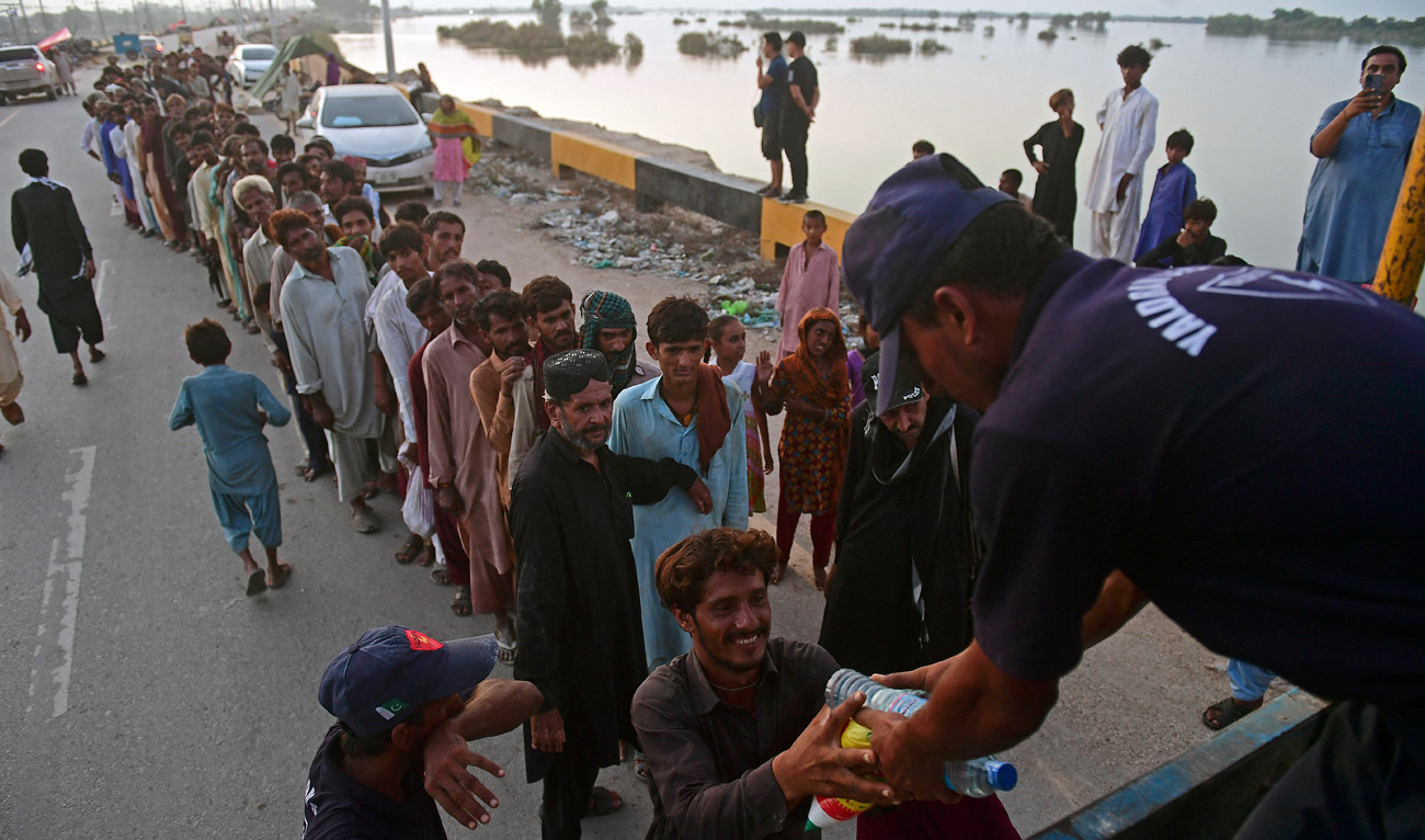 Internally displaced flood-affected people stand in a queue while waiting to receive relief food packets in the flood-hit area of Sukkur in Sindh province on August 31, 2022. (AFP)