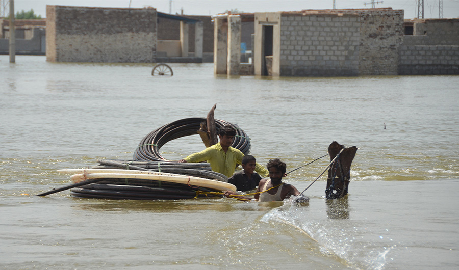 Flood-affected people shift materials across a flooded area at Dera Allah Yar town in Jaffarabad district, Balochistan province, on September 6, 2022. (AFP)