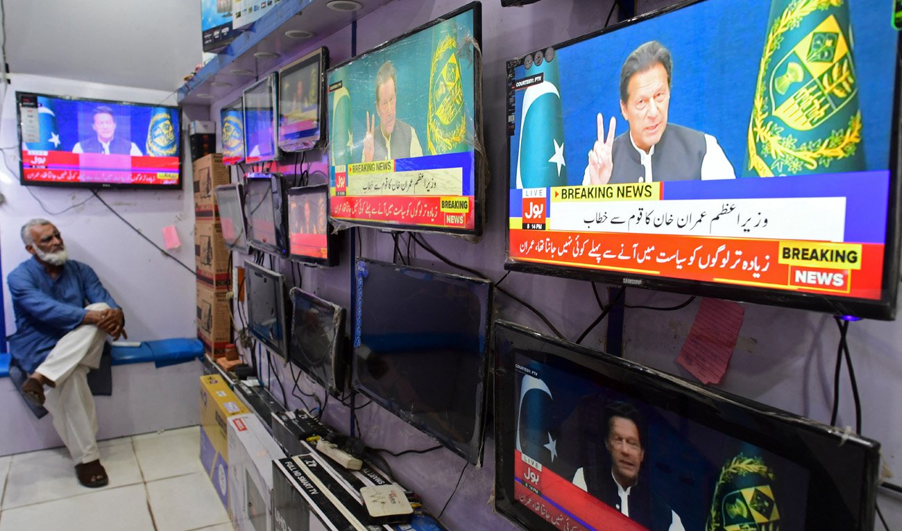 A man listens to Pakistan's then Prime Minister Imran Khan addressing the nation on television at a market in Karachi on March 31, 2022. (AFP/File)