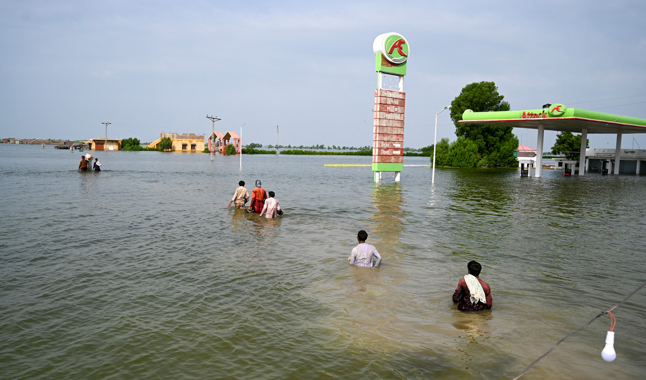 Internally displaced people wade through floodwaters to return home after heavy monsoon rains in Dadu district, Sindh province on September 7, 2022. (AFP)