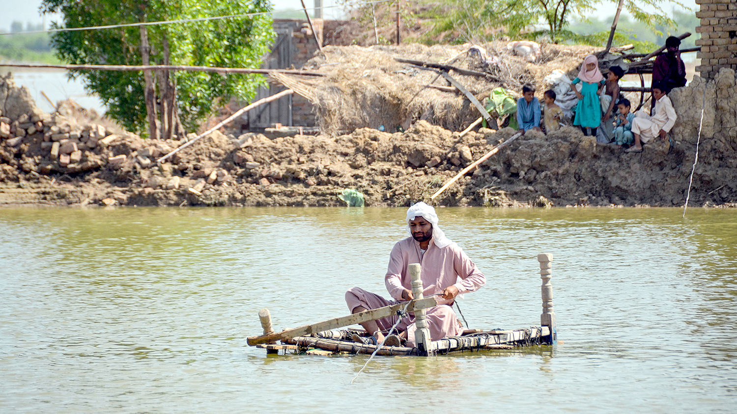 A flood-affected man uses a makeshift raft to cross s stream of flood waters near his damaged house in Jaffarabad district of Pakistan's Balochistan province on September 23, 2022. (AFP)