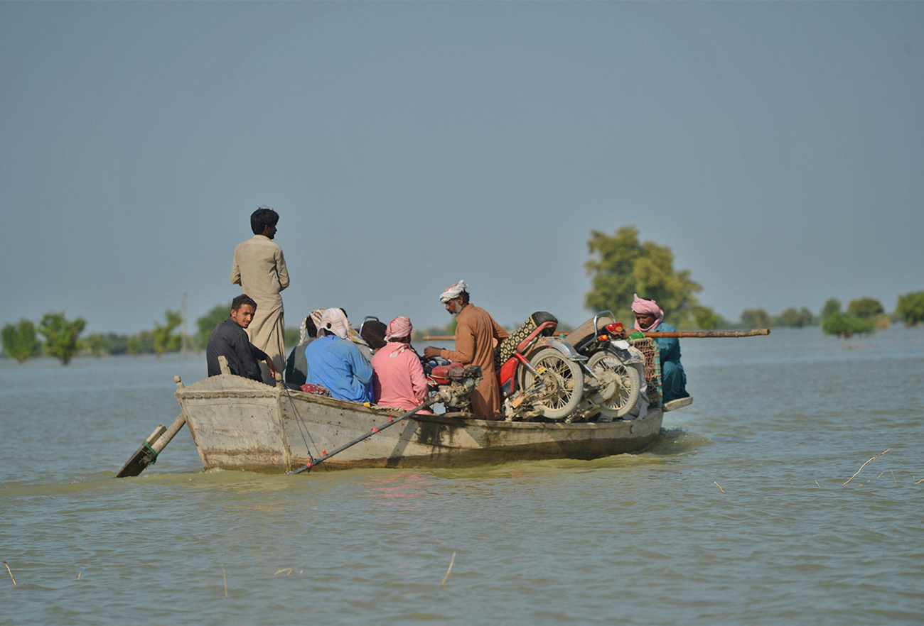 Internally displaced people use boats to cross the flooded area in Dadu district, Pakistan Sindh province on September 27, 2022. (AFP)