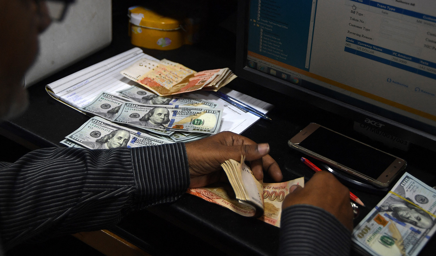 A dealer counts Pakistani currency notes next to US dollars at a currency exchange shop in Karachi on April 15, 2019. (AFP/File)
