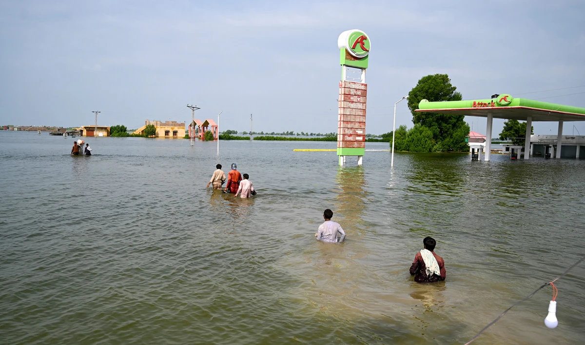 Internally displaced people wade through floodwaters to return home after heavy monsoon rains in Dadu district, Sindh province on September 7, 2022. (AFP)