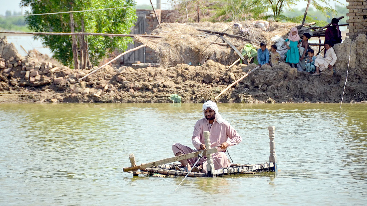 A flood-affected man uses a makeshift raft to cross s stream of flood waters near his damaged house in Jaffarabad district of Pakistan's Balochistan province on September 23, 2022. (AFP)