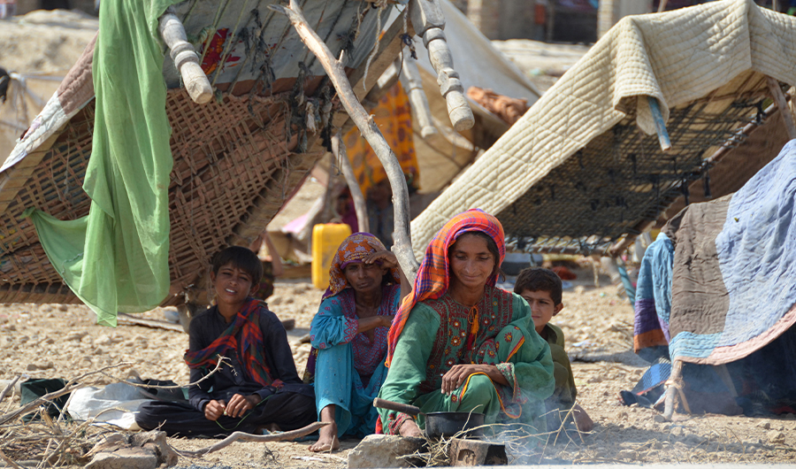 A displaced flood-affected family sits under the shade of a cot bed at Dera Allah Yar in Jaffarabad district of Balochistan province on September 20, 2022. (AFP)