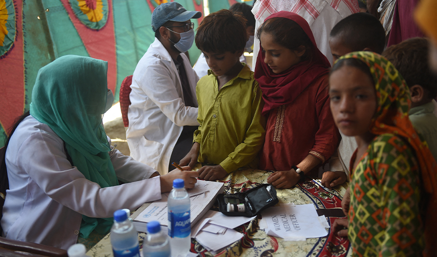 Children displaced by floods gather around a paramedic at a makeshift medical camp set in Dadu district, Sindh province on September 27, 2022. (AFP)