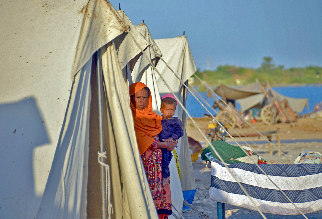 A displaced flood-affected woman stands with her child at a makeshift camp alongside flood waters at Dera Allah Yar in Jaffarabad district of Balochistan province, Pakistan, on October 5, 2022. (AFP)