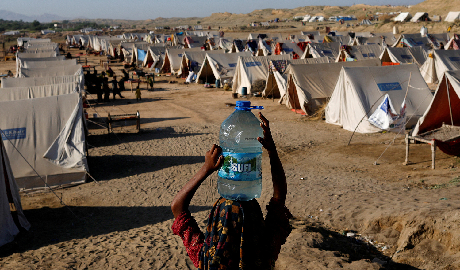 A displaced girl carries a bottle of water she filled from nearby stranded flood-waters, as her family takes refuge in a camp, in Sehwan, Pakistan, on September 30, 2022. (REUTERS)
