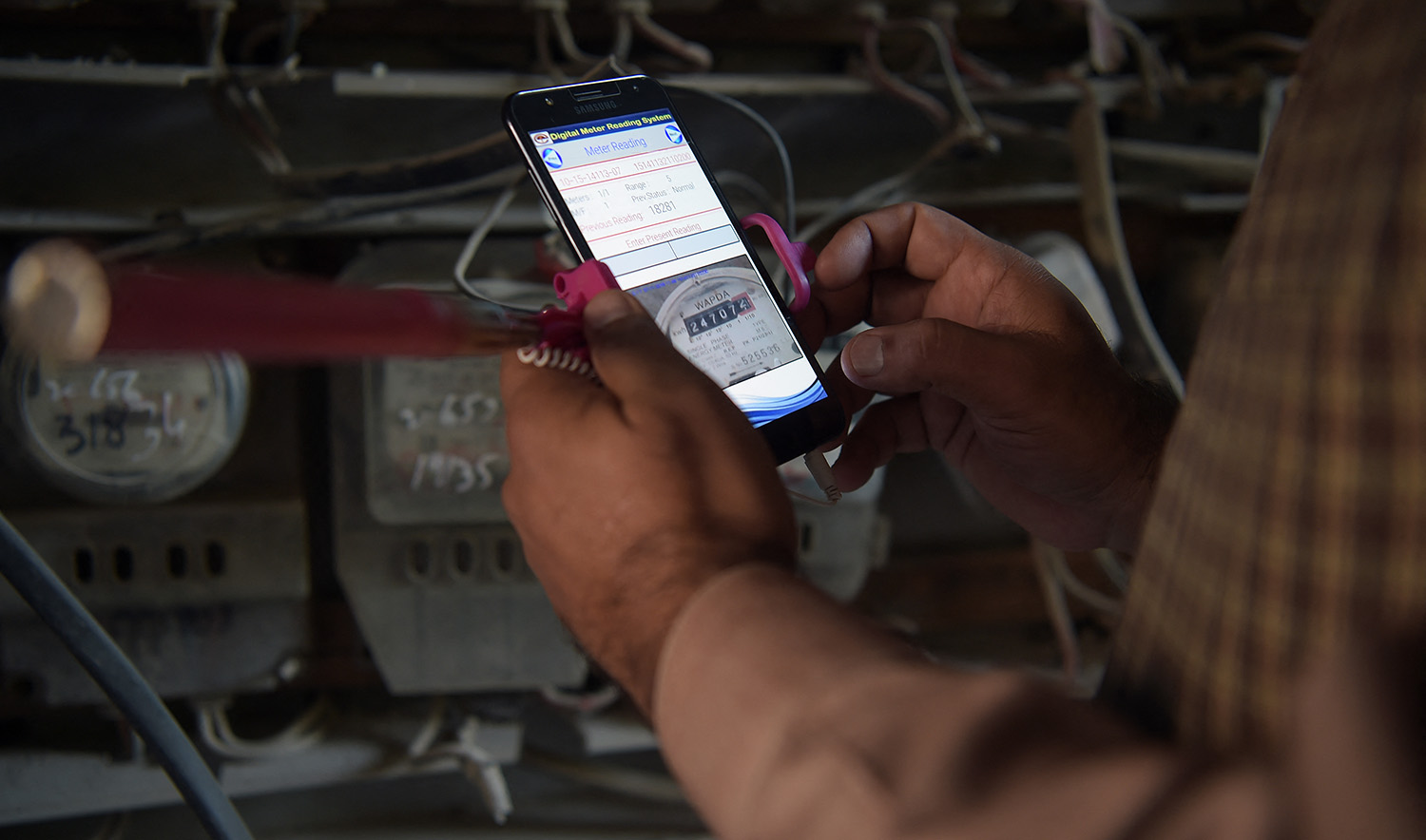 Muhammad Noshad, a Pakistani employee of the state-run Islamabad Electric Supply Company (IESCO), takes a meter reading with his smartphone at a commercial building in Islamabad on November 7, 2018. (AFP/File)