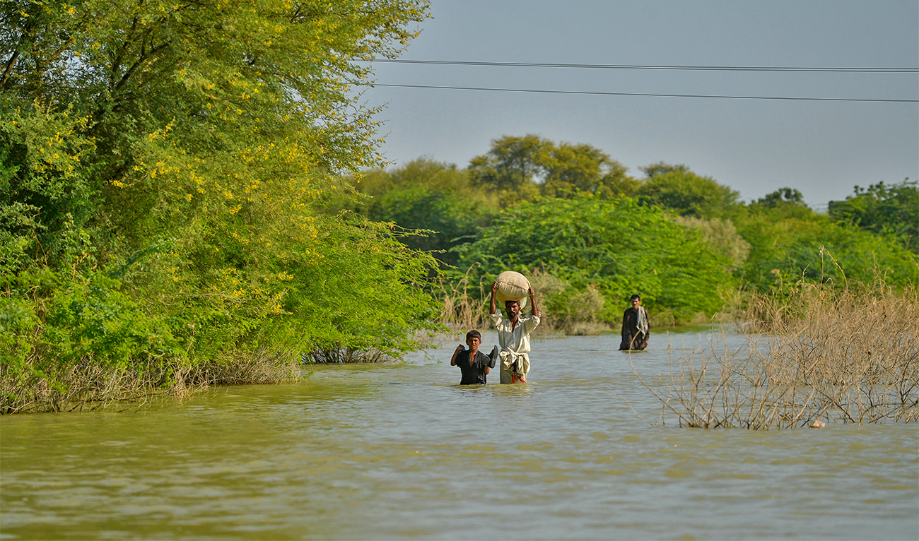Internally displaced flood-affected people wade through a flooded area in Dadu district of Pakistan's Sindh province on September 27, 2022. (AFP)
