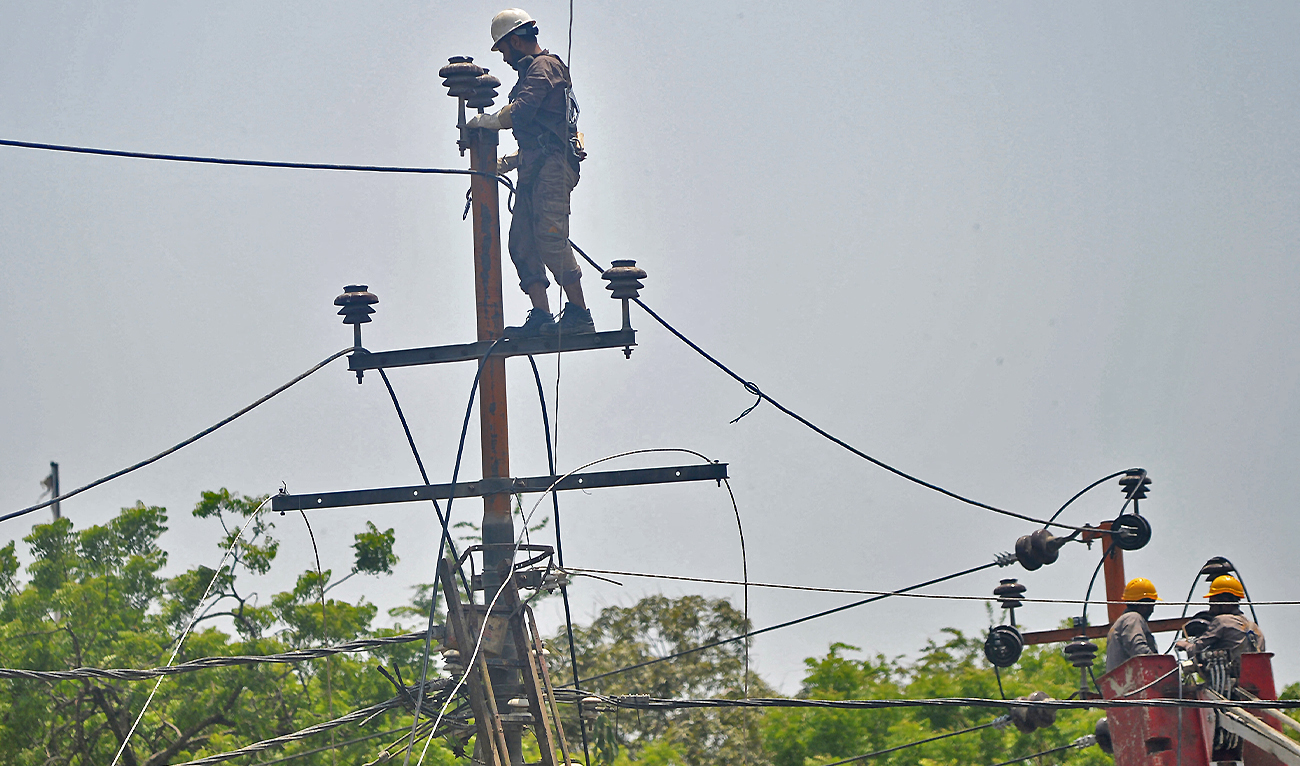 Men work on electric pylons along the roadside in Karachi on May 30, 2021. (AFP/File)