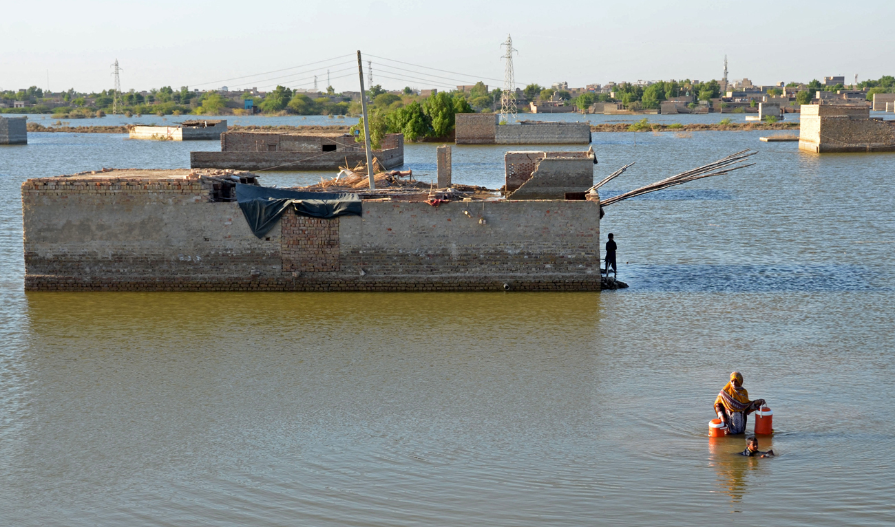 In this file photo taken on October 06, 2022 A flood-affected woman wades through the flood waters to fill drinking water at Dera Allah Yar in Jaffarabad district of Balochistan province. (AFP)