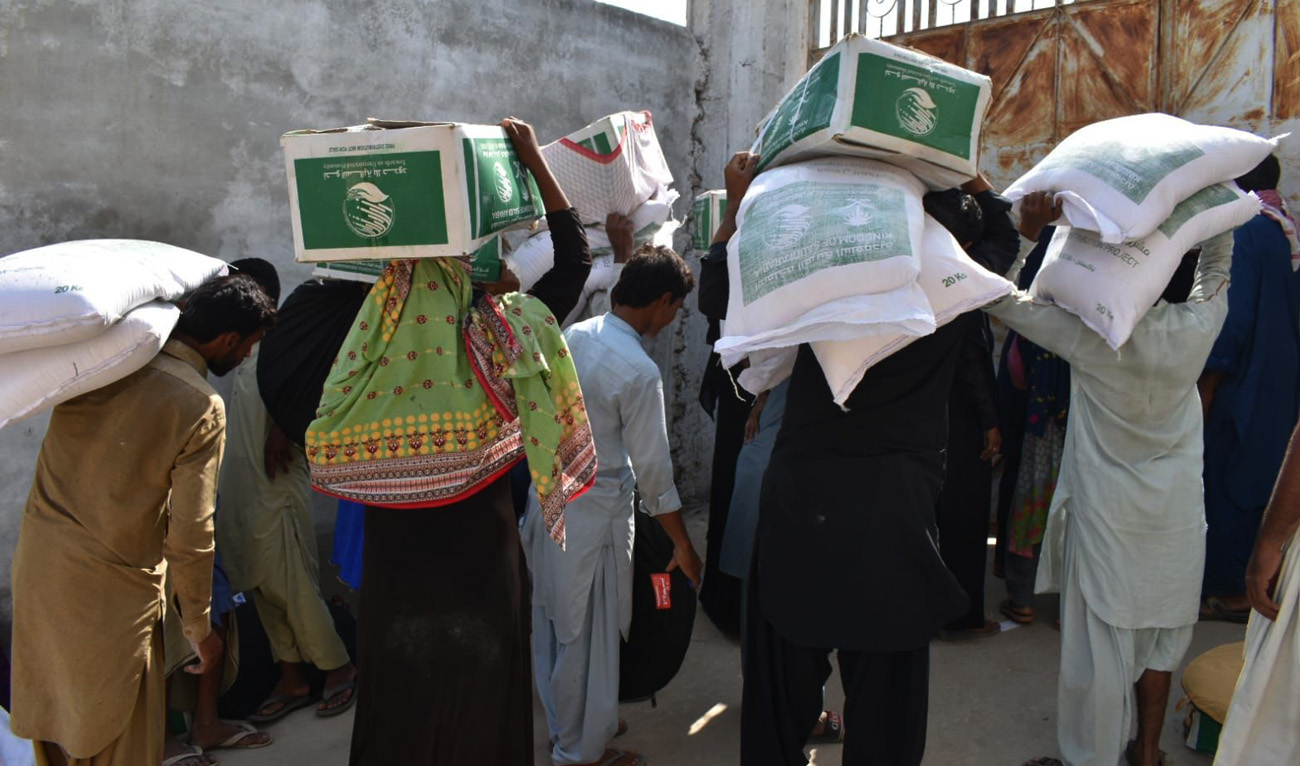 Flood-affected people carry food packages distributed by Saudi Arabia’s King Salman Humanitarian Aid and Relief Center in Pakistan's Sindh province on October 12, 2022. (Twitter/KSRelief)