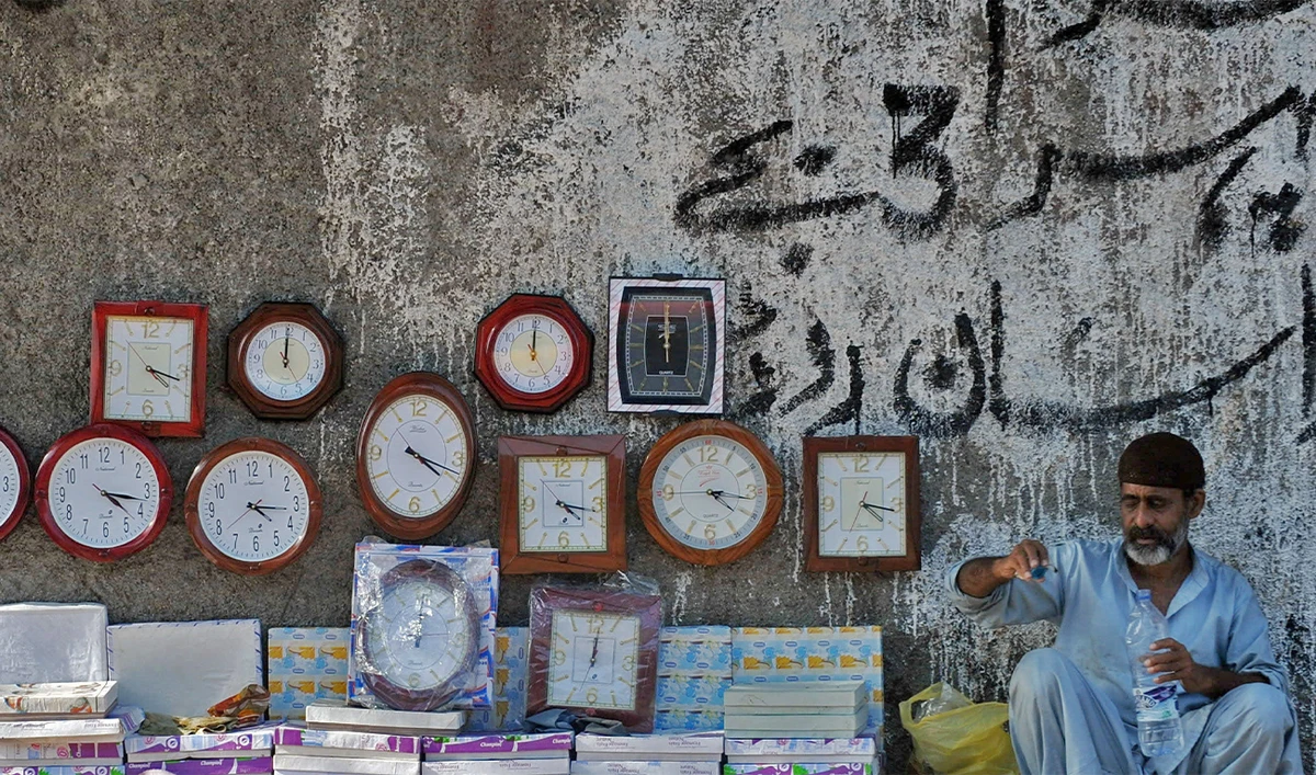 A Pakistani vendor (R) waits for customers as he sells cheap clocks on a footpath in Saddar bazaar, a neighbourhood of Karachi, on March 15, 2010. (AFP/File)