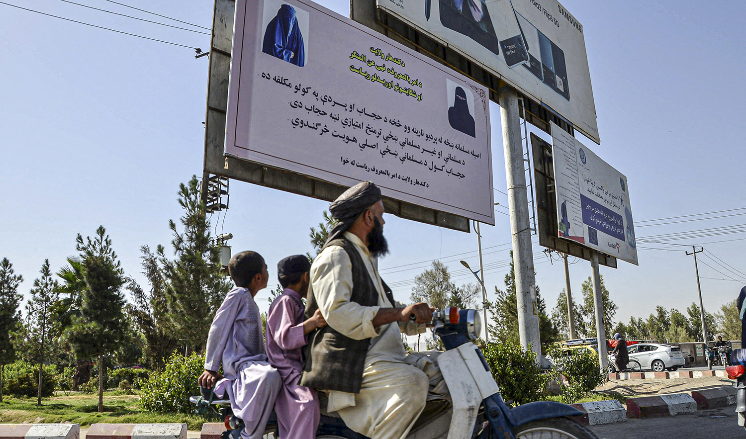 People ride a motorbike past a banner placed by Taliban authorities asking women to wear a hijab, in Kandahar on June 16, 2022. (AFP/File)