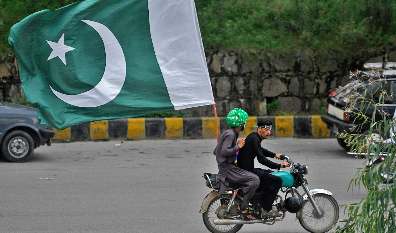Men ride on a bike with a large flag of Pakistan along a street in Islamabad, Pakistan, on August 14, 2020. (AFP/File)