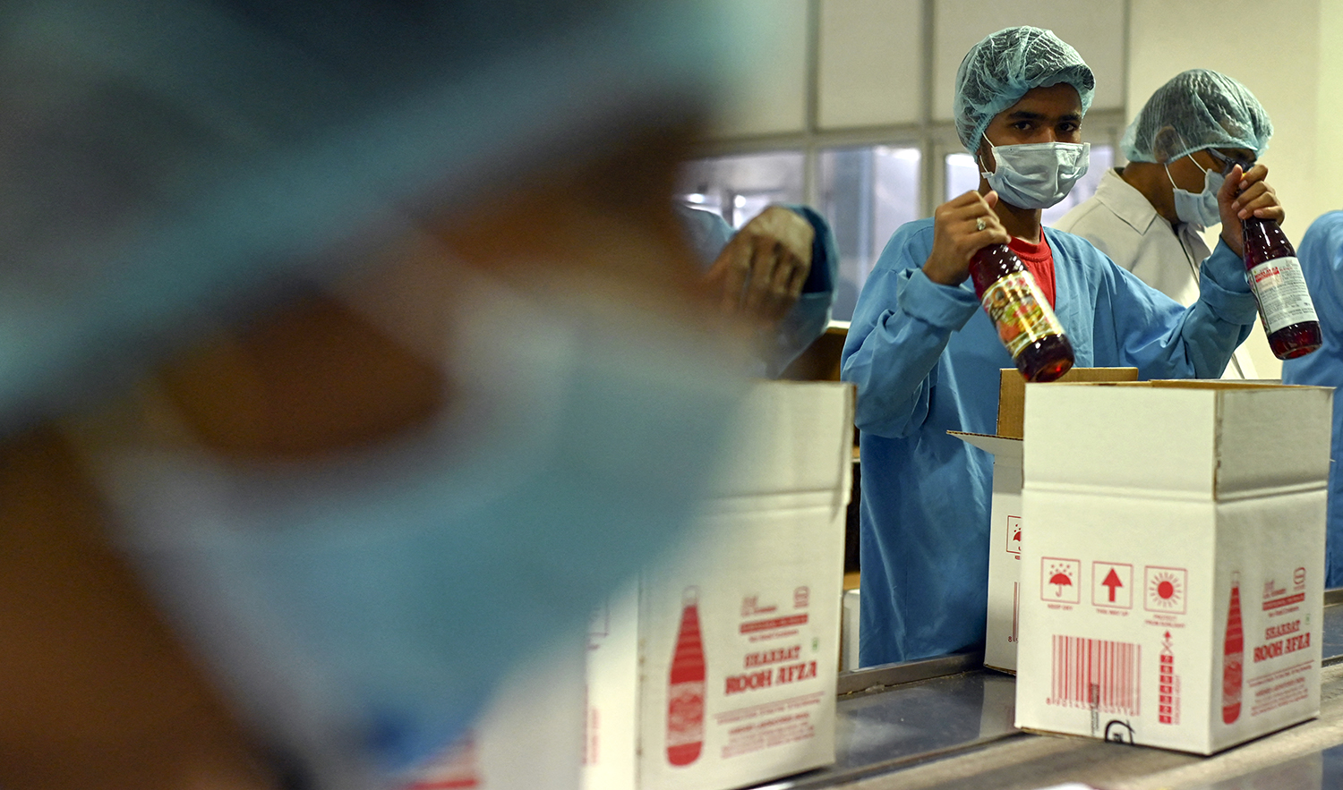 Employees pack bottles of Rooh Afza beverages in cardboard boxes at the end of the assembly line at Hamdard Laboratories factory in Manesar, India on May 21, 2022. (AFP/File)