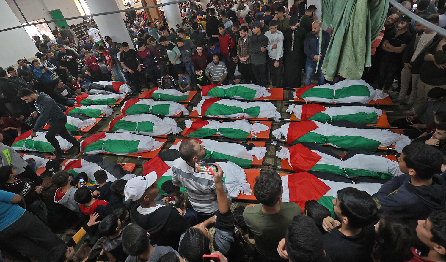 Palestinians carry the flag-draped bodies of people who died a day earlier, when fire broke out in an apartment, in the Jabalia refugee camp in the northern Gaza strip, on November 18, 2022. (AFP)