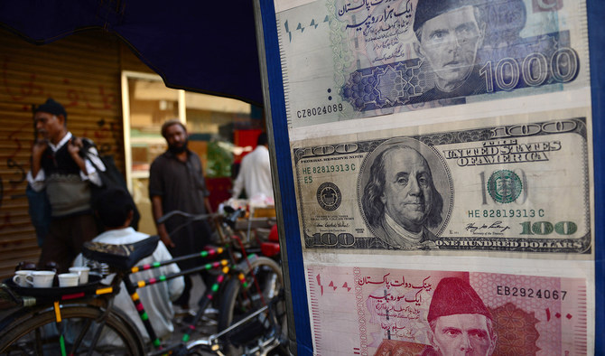 Pakistani pedestrians walk past a roadside currency exchange stall displaying examples of Pakistani and US currency notes in Karachi on February 11, 2013. (AFP/File)