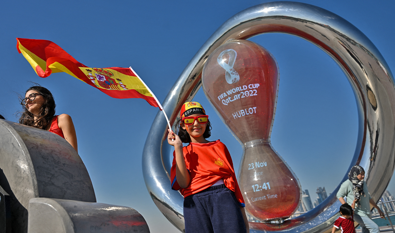 A child holds Spain's national flag in front of the countdown clock of the Qatar 2022 World Cup football tournament in Doha on November 23, 2022. (AFP)