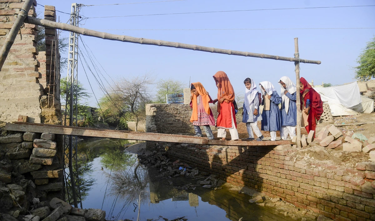 In this picture taken on October 28, 2022, students walk across a metal girder atop floodwaters in Chandan Mori, in Dadu district of Sindh province. (Photo courtesy: AFP/File)