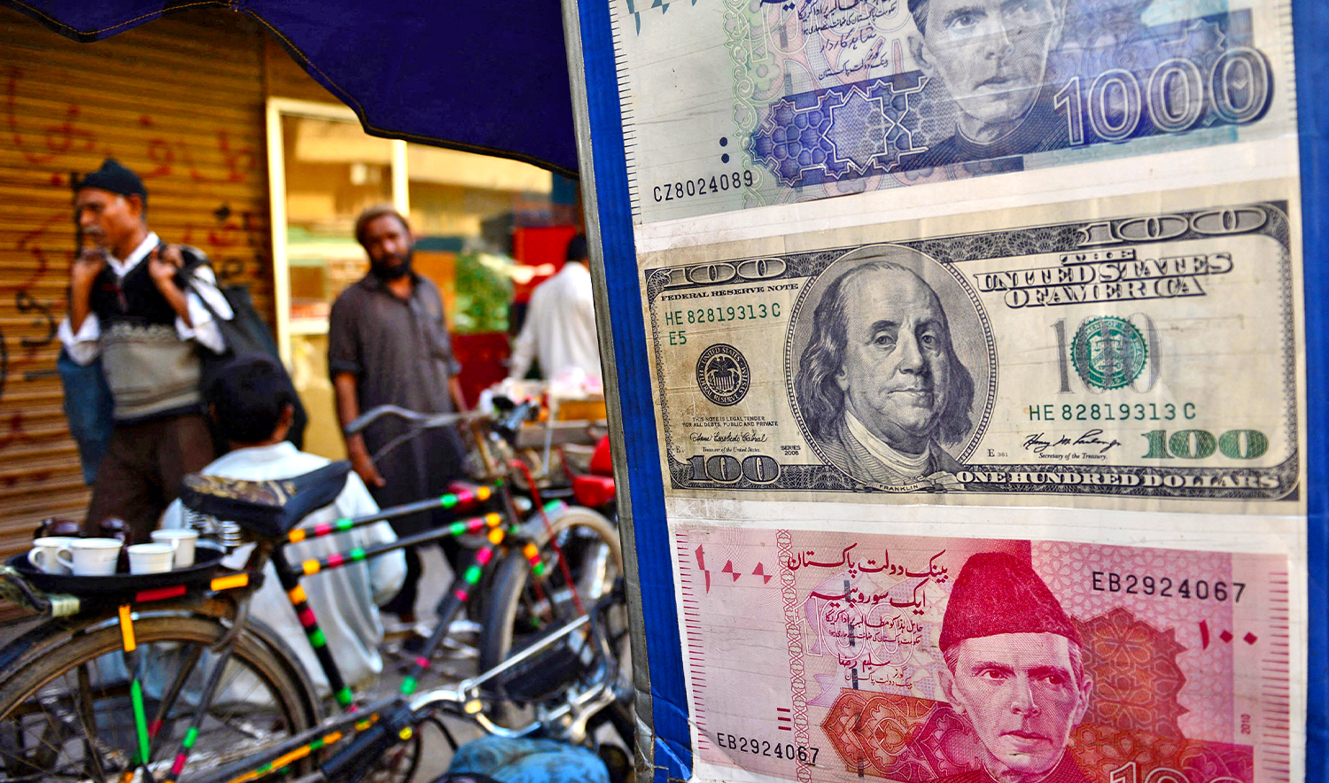 Pakistani pedestrians walk past a roadside currency exchange stall displaying examples of Pakistani and US currency notes in Karachi on February 11, 2013. (AFP/FILE)