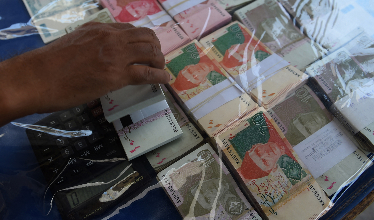In the file picture taken on May 13, 2019, a currency exchange vendor adjusts Pakistani currency notes as he waits for customers on a street in Karachi. (Photo courtesy: AFP/File)
