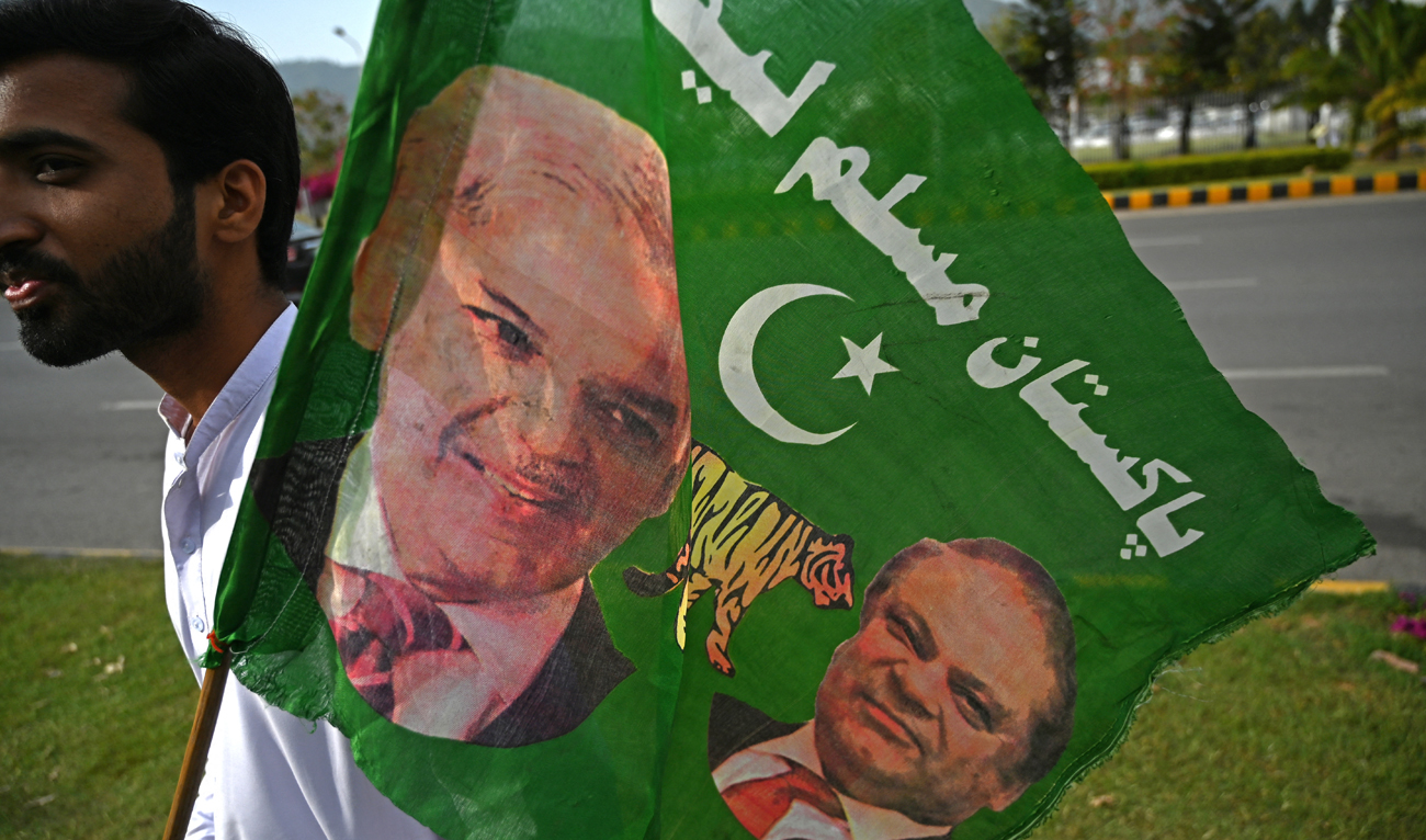A supporter of Pakistan Muslim League-N (PML-N) holds a party flag with images of Shehbaz Sharif and his elder brother and former prime minister Nawaz Sharif outside the parliament house building in Islamabad on April 11, 2022. (Photo courtesy: AFP/File)