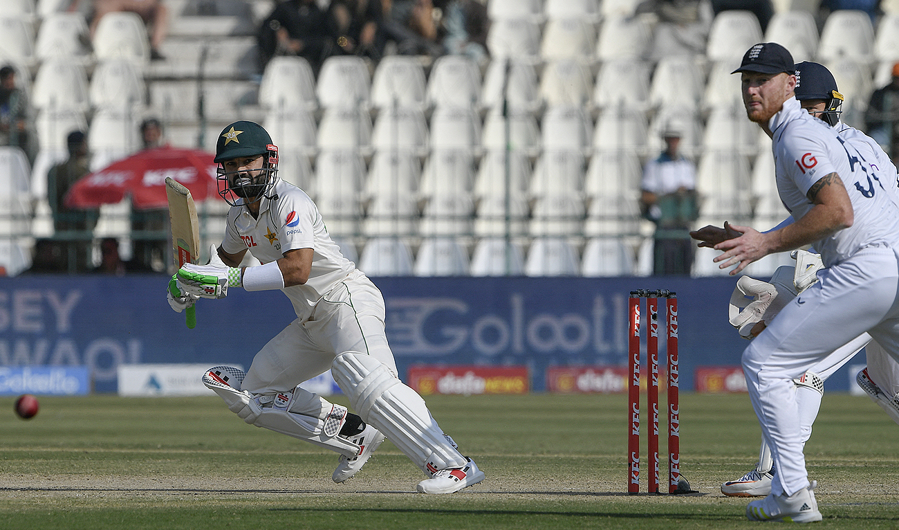 Pakistan's Mohammad Rizwan (L) plays a shot as England's captain Ben Stokes (R) watches during the third day of the second cricket Test match between Pakistan and England at the Multan Cricket Stadium in Multan on December 11, 2022. (Photo courtesy: AFP)