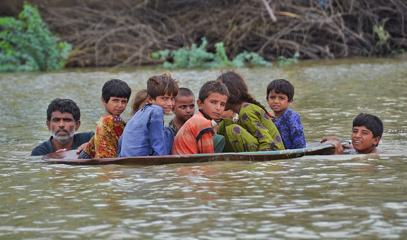 A man (L) along with a youth use a satellite dish to move children across a flooded area after heavy monsoon rainfalls in Jaffarabad district, Balochistan province, on August 26, 2022. (AFP)