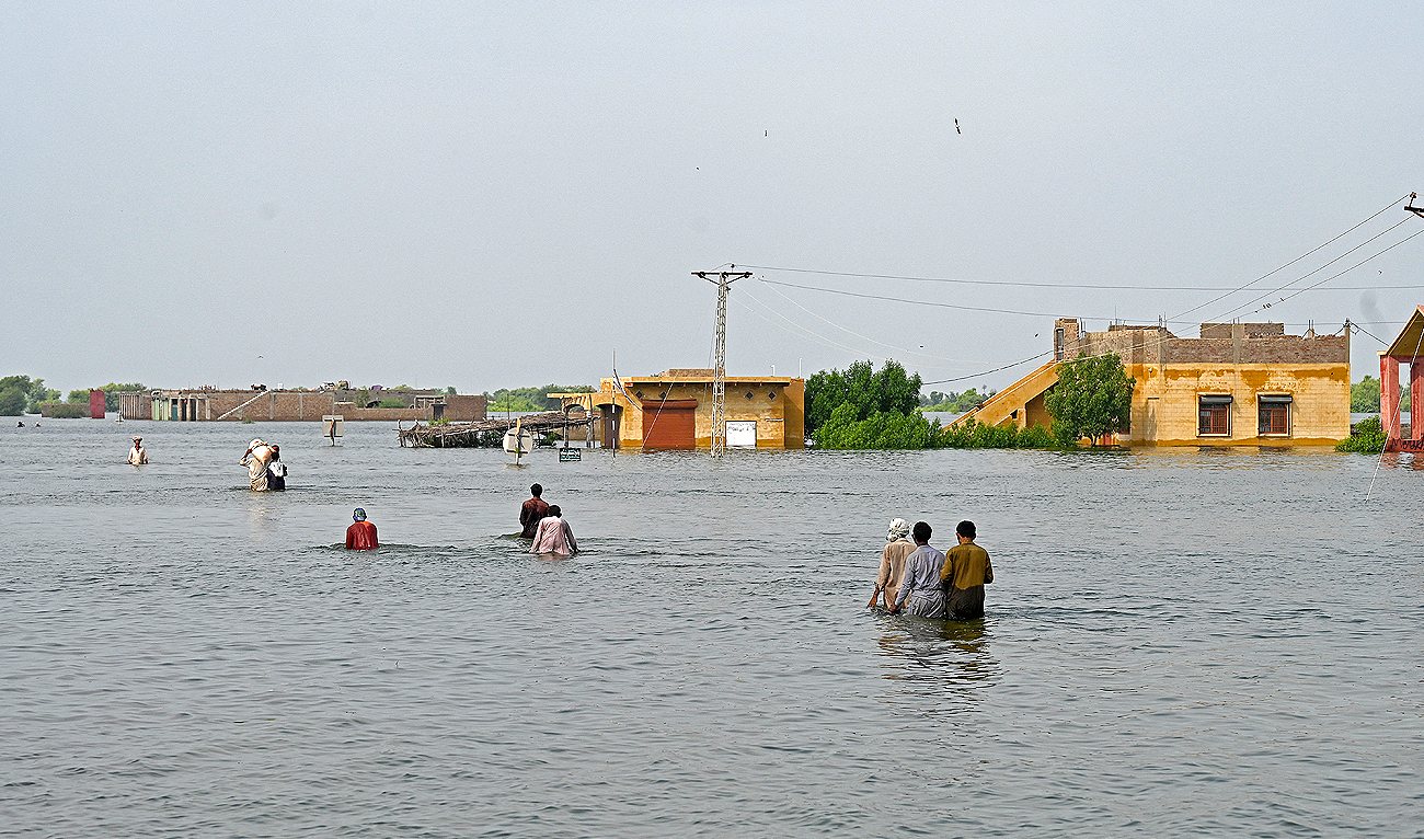 In this file picture taken on September 7, 2022, internally displaced people wade through floodwaters to return home following heavy monsoon rains in Dadu district, Sindh province. (Photo courtesy: AFP/File)