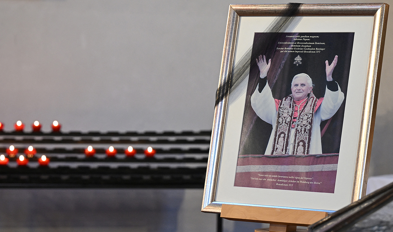 Candles are seen near a picture of late former Pope Emeritus Benedict XVI in the Catholic St Oswald church in his birth place Marktl, southern Germany, on December 31, 2022. (Photo courtesy: AFP)