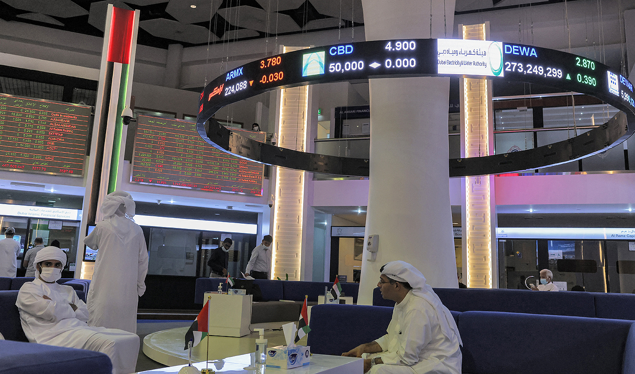 People sit under a display showing the values of different stocks at the Dubai Financial Market stock exchange in the Gulf emirate on April 12, 2022. (Photo courtesy: AFP/File)