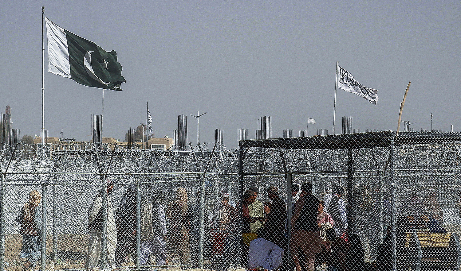 Afghan and Pakistani nationals walk through a security barrier to cross the border as a national flag of Pakistan and a Taliban flag is masted in the Pakistan-Afghanistan border crossing point in Chaman on August 24, 2021. (AFP/File)