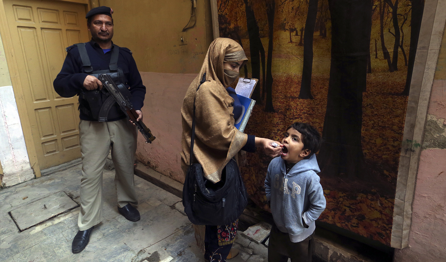 A police officer stands guard while a health worker gives a polio vaccine to a child in Peshawar, Pakistan, on December 5, 2022. (AP/File)